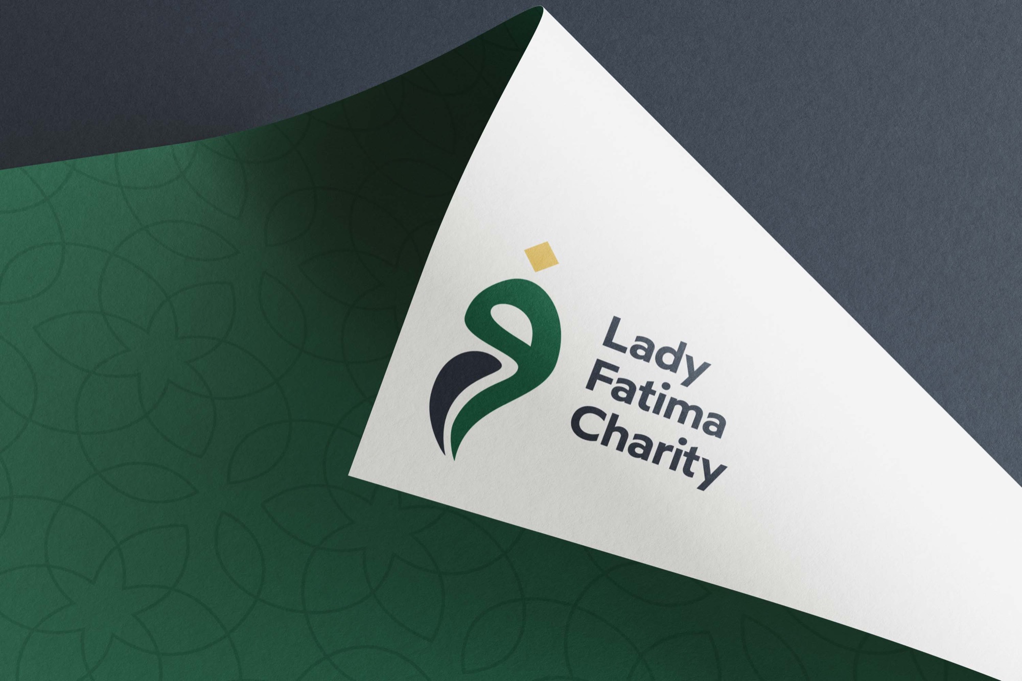 Lady Fatima Charity — the logo debossed on folded white paper over Saadat Green
