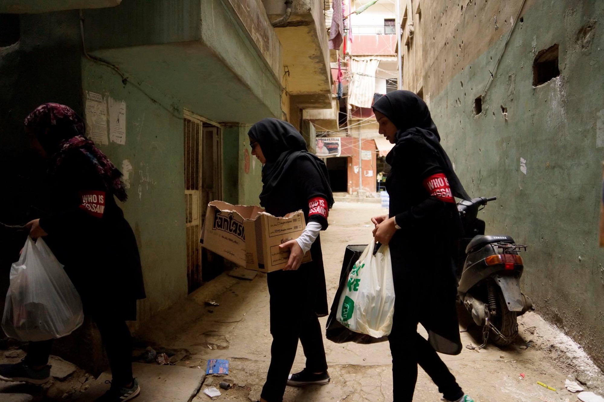 Who is Hussain — volunteers delivering aid parcels through a narrow alley